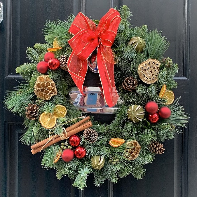 Christmas wreath with red ribbon, cinnamon sticks, baubles and pine cones hanging on front door
